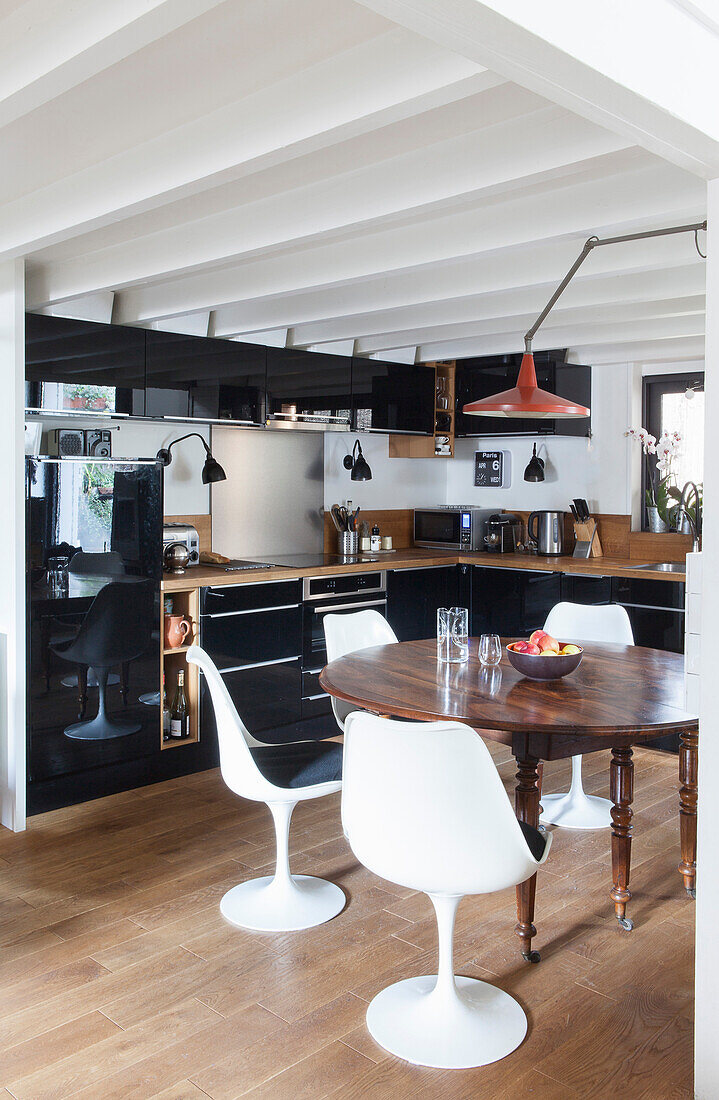 Open kitchen and dining area with antique wooden table and white modern chairs in a loft