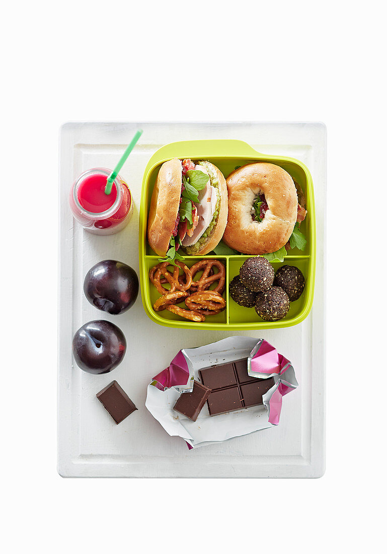 Teenager-Lunchbox mit belegtem Bagel, Getränk, Obst und Schokolade