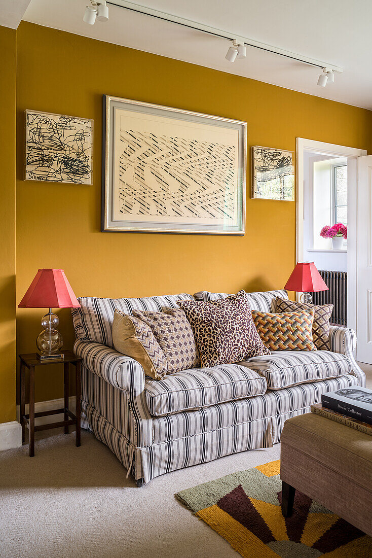 Sofa mit gestreiftem Bezug und Kissen im Salon mit senfgelber Wand