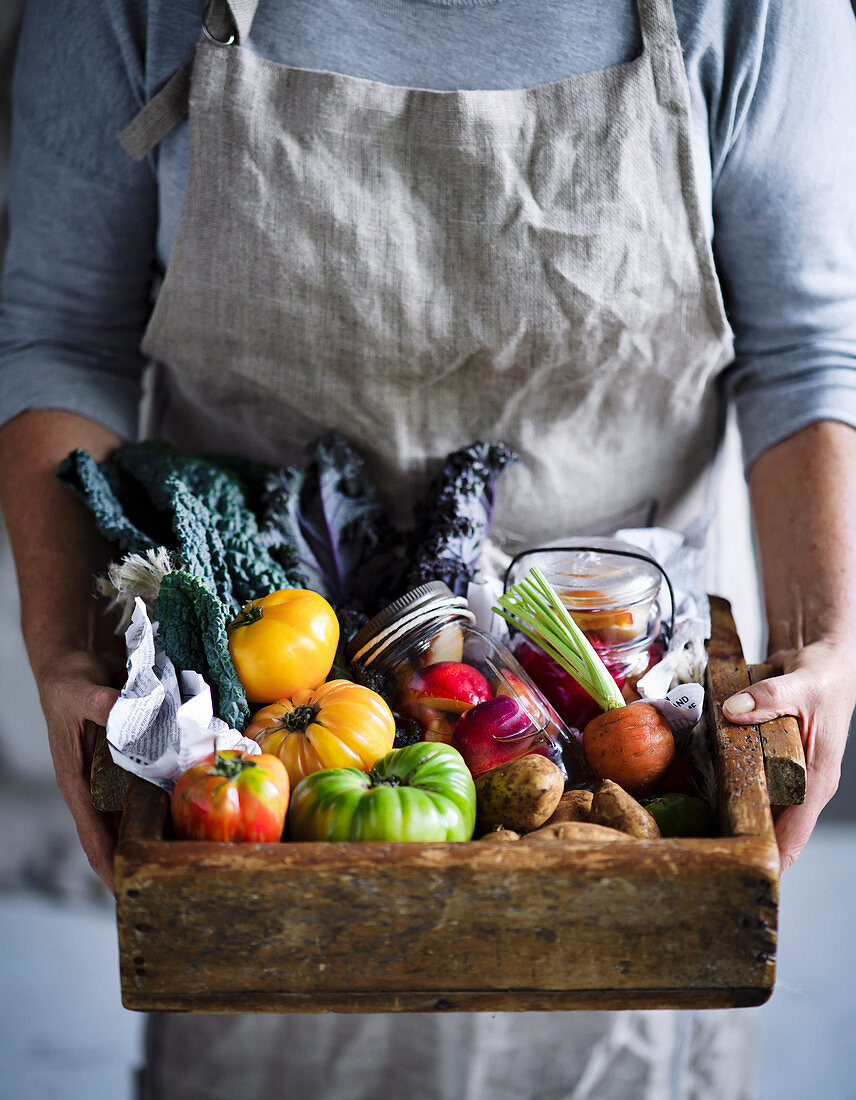 Hands holding wooden box with fresh vegetables