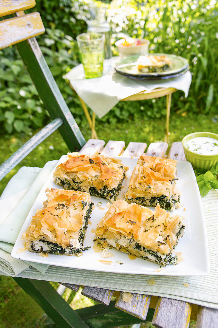 Leichte Spanakopita auf Servierplatte im sommerlichen Garten