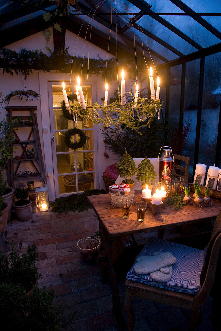 Hängender Kranz mit brennenden Kerzen über Esstisch in weihnachtlich dekoriertem Wintergarten