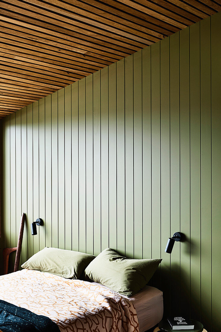 Doppelbett im Schlafzimmer mit grün gestrichener Holzverkleidung