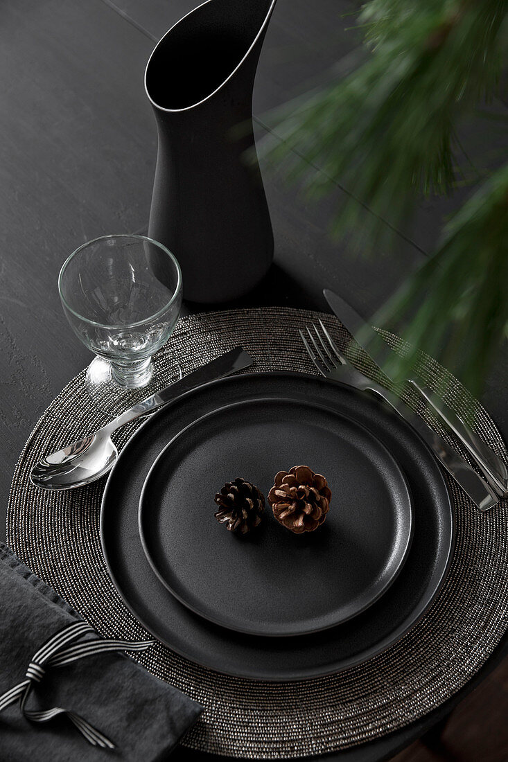 Black place setting decorated with conifer cones