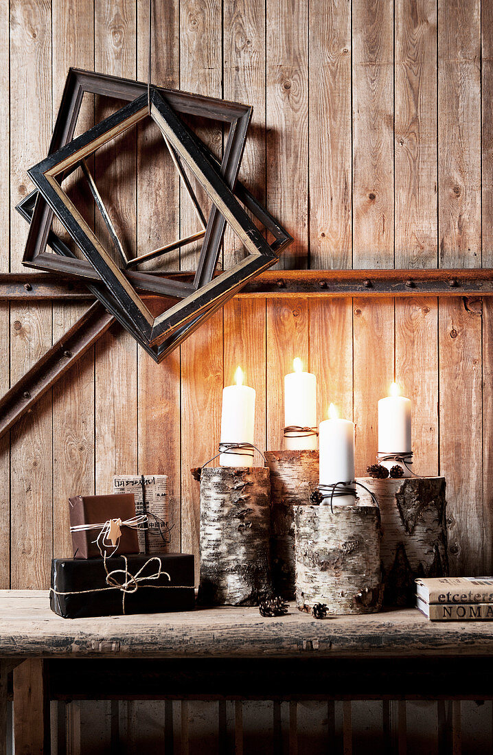 Lit candles on wooden bench below old picture frames on rustic board wall