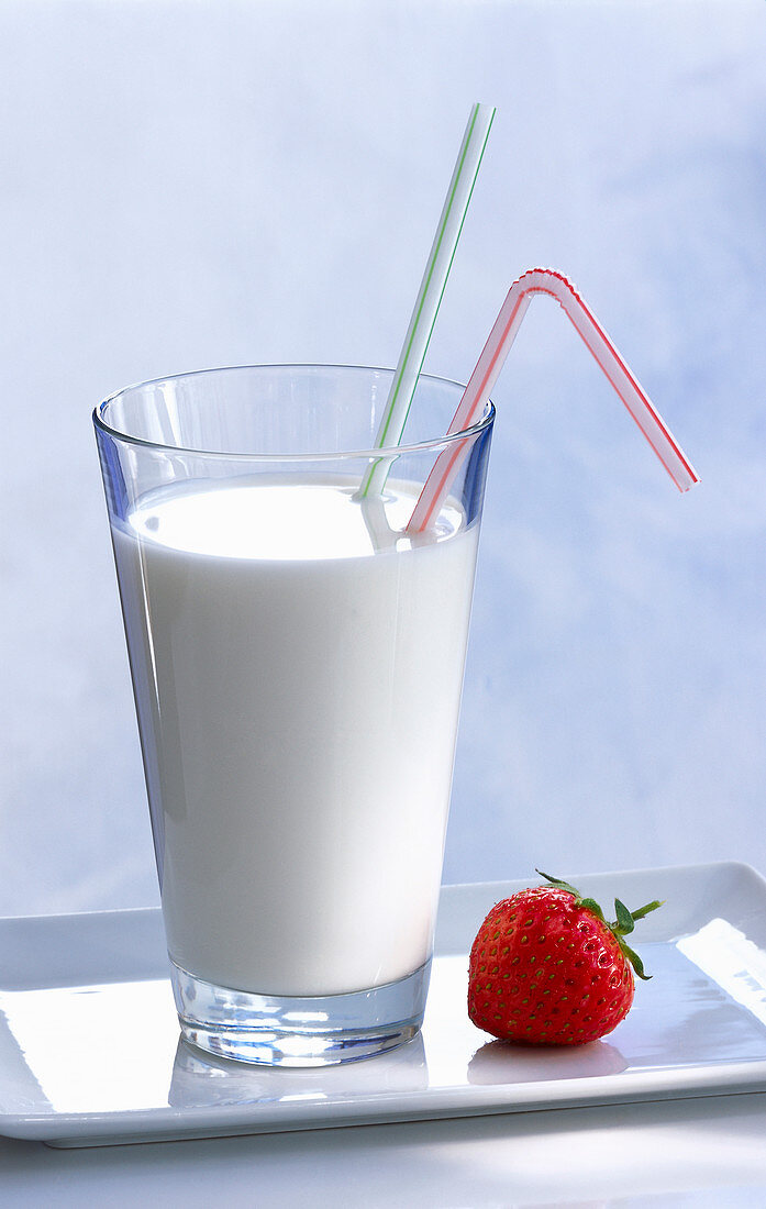 Ein Glas Milch mit zwei Strohhalmen, daneben eine Erdbeere