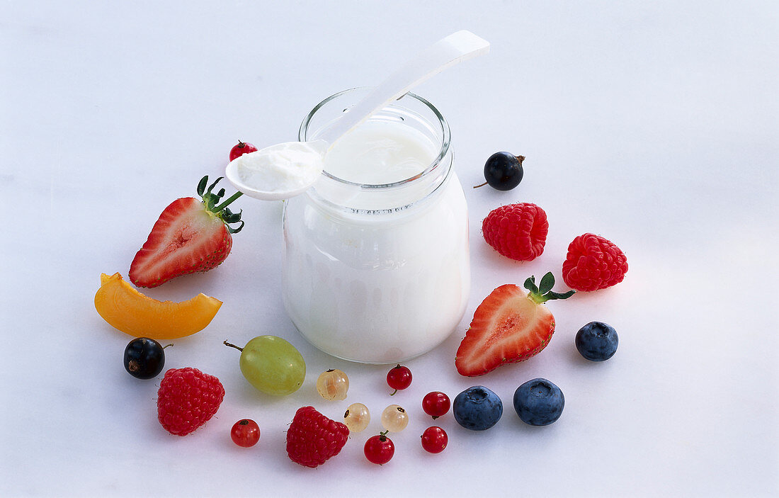 Ein Glas Joghurt mit Löffel, umgeben von Beeren