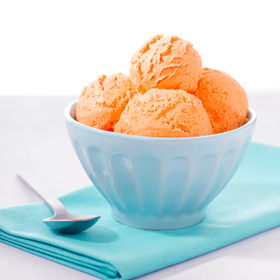 Close-up of 4 scoops of orange colored ice cream in blue bowl