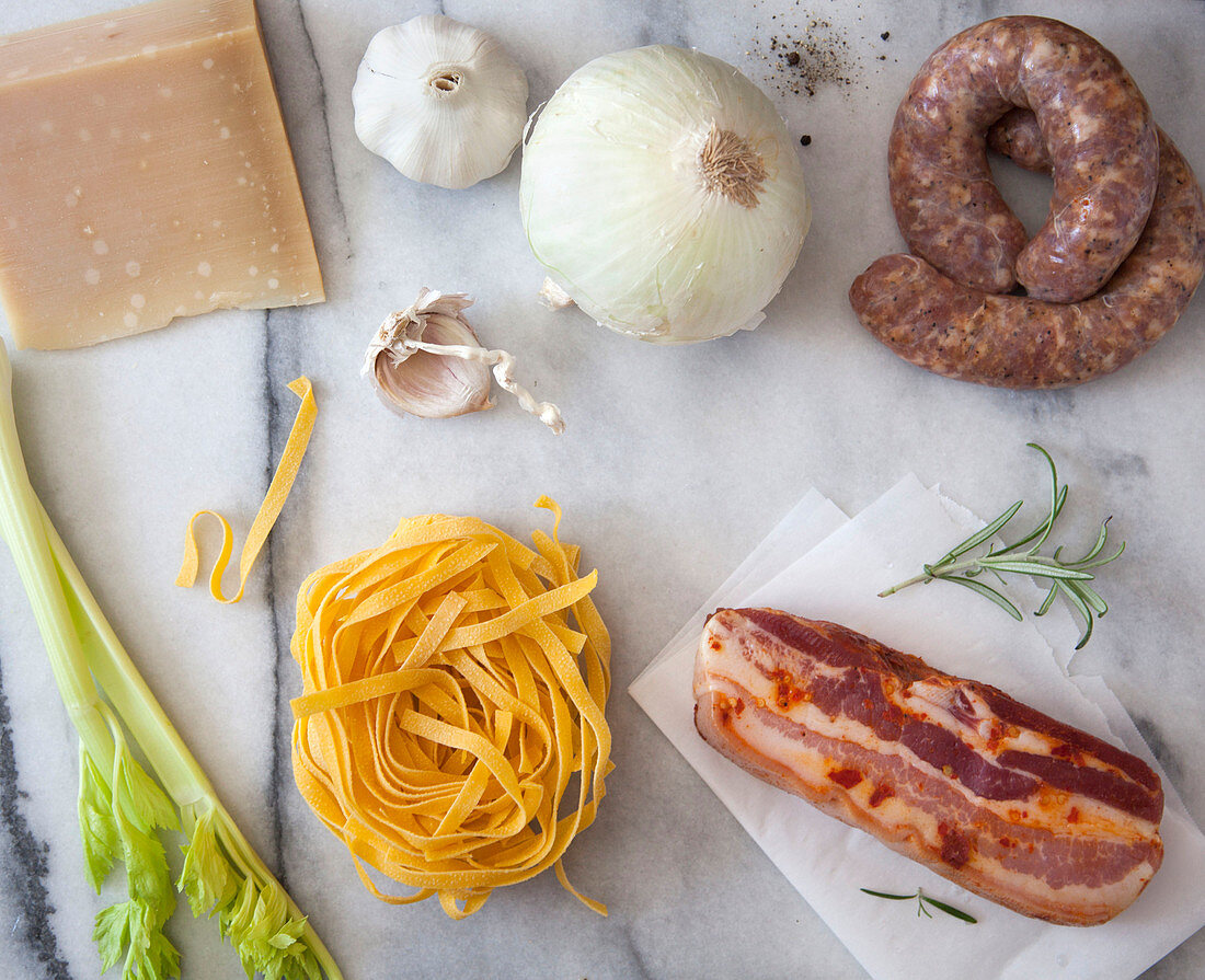 Pasta ingredients - parmesan cheese, white onion, sausage, garlic, rosemary, cured bacon, egg noodles and celery