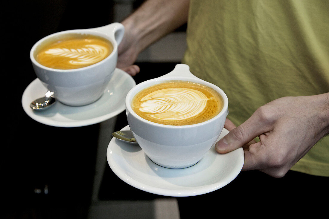 Male barista holding two latte coffees with latte art