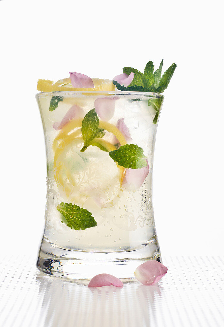 Cocktail drink with lemon twist, rose petals and mint leaves