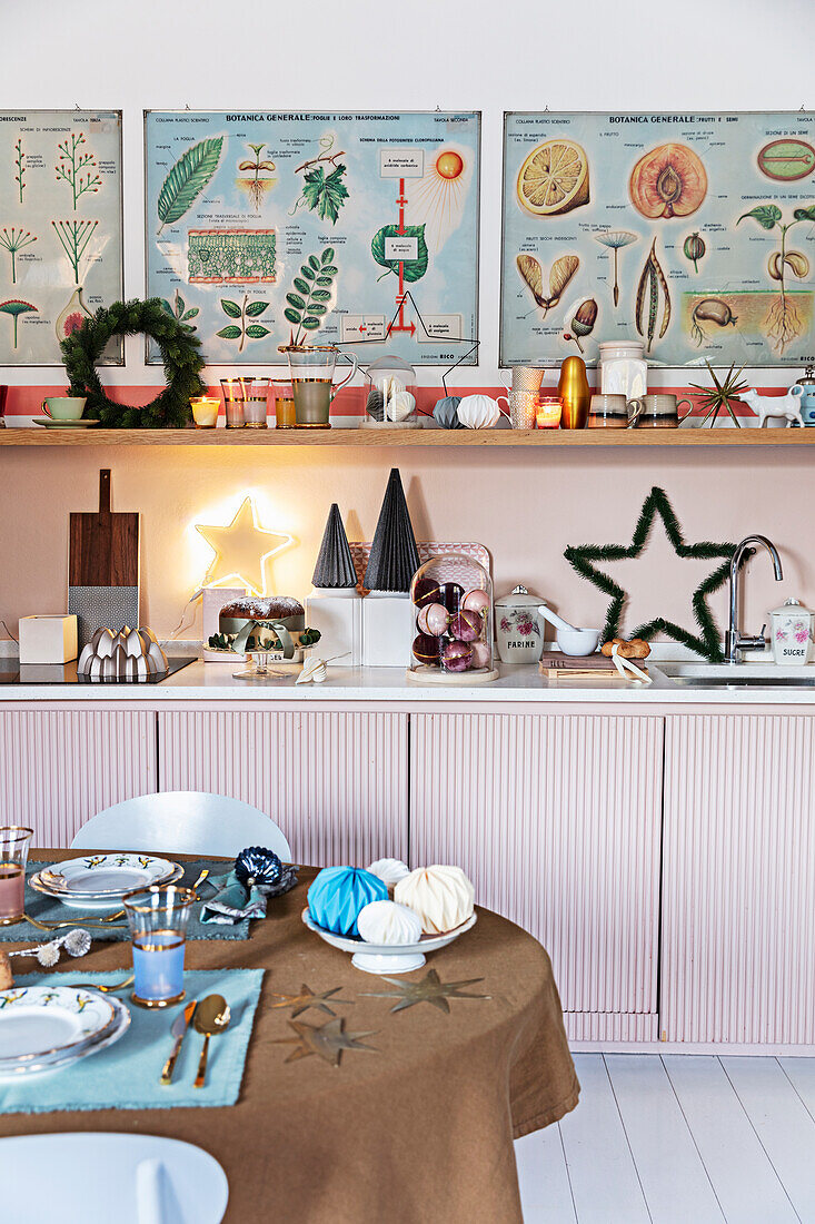 View of the fitted kitchen cabinets with pink fronts and shelves above the laid Christmas table