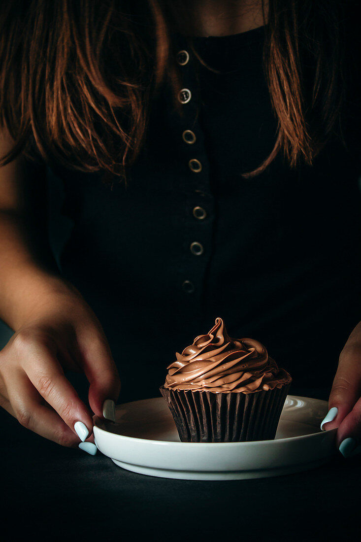 Frau hält Teller mit Schokoladen-Cupcake