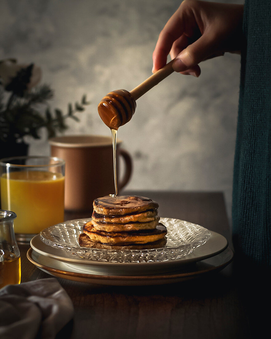 Frau träufelt Honig auf Pancake-Stapel
