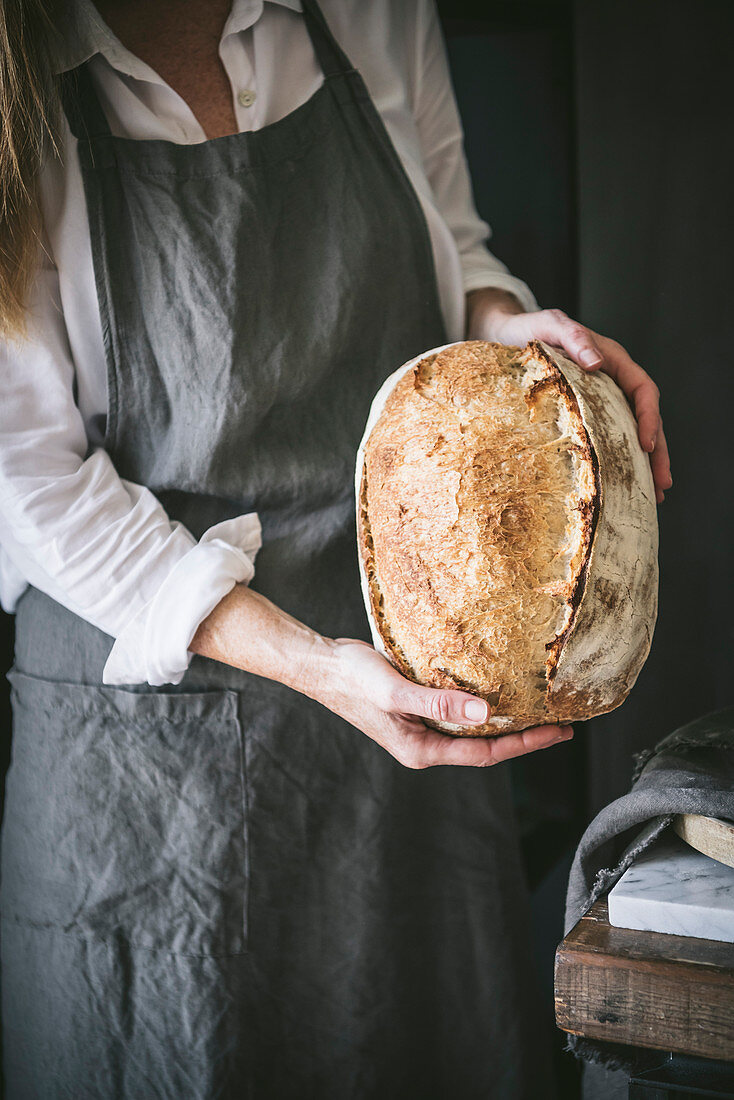Woman holds homemade sourdough bread in hands