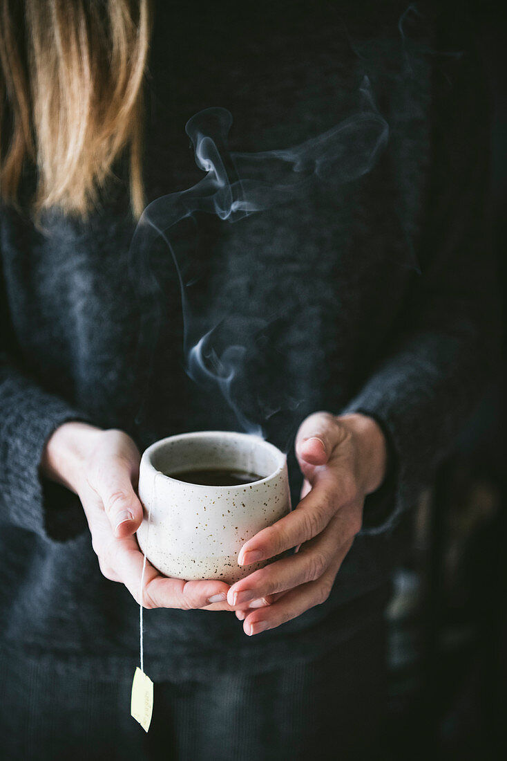 Frau hält eine dampfende Tasse schwarzen Tee