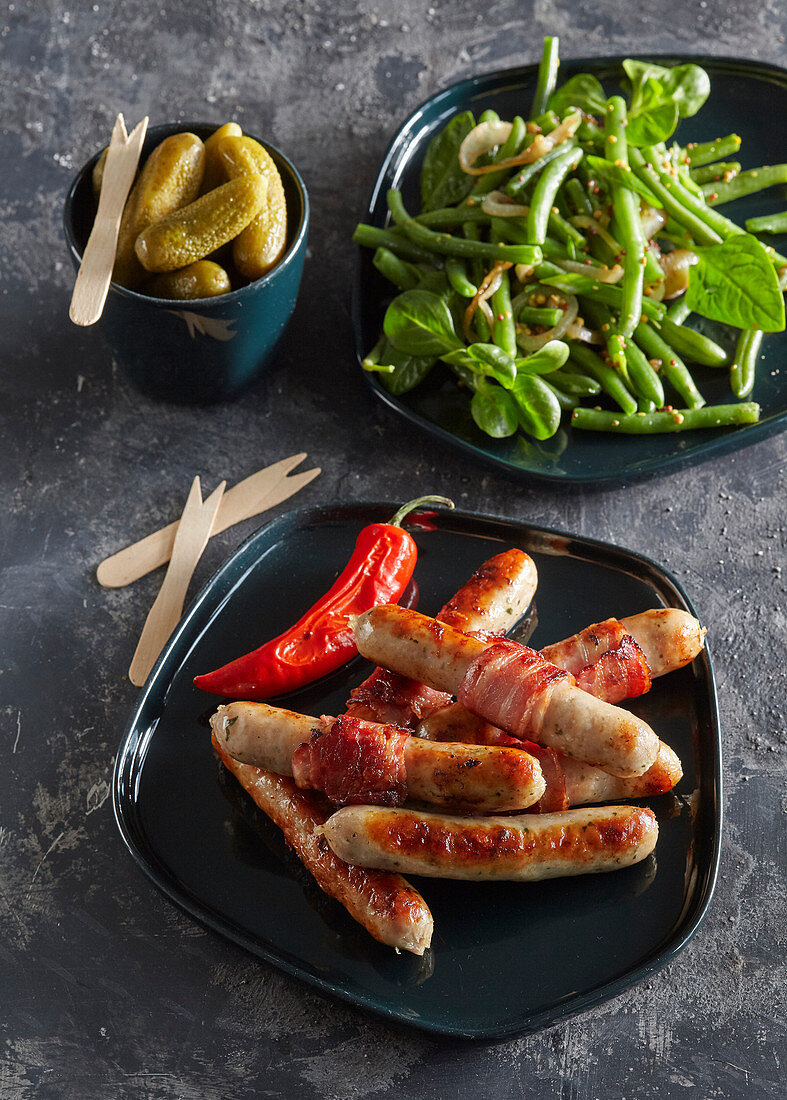 Sausages in striped bacon with green beans