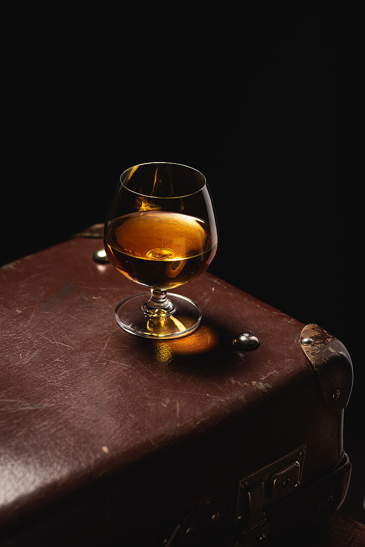 Cognac im Schwenker auf Vintage-Koffer