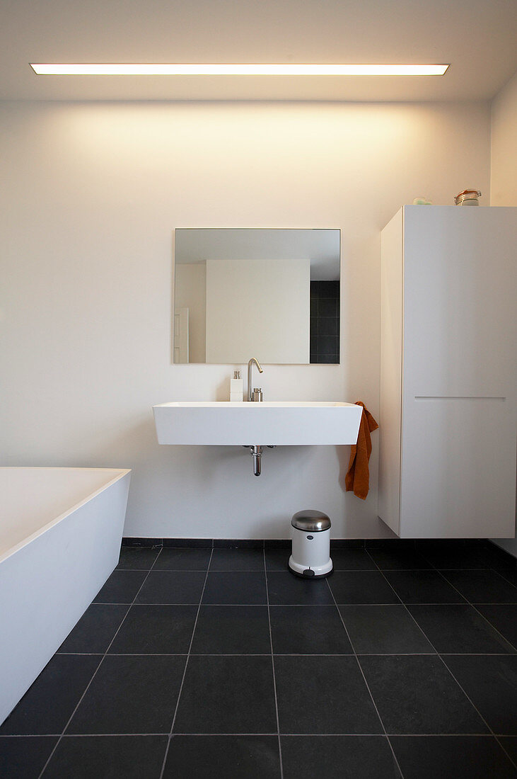 Weißes Waschbecken, Schrank und Badewanne im Badezimmer mit schwarzem Fliesenboden