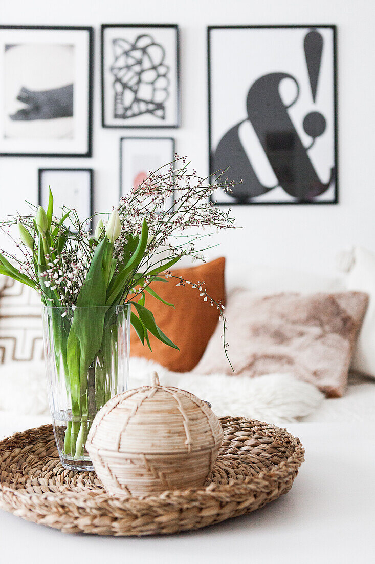 Bouquet of tulips and box on wicker tray, modern pictures on wall in the background