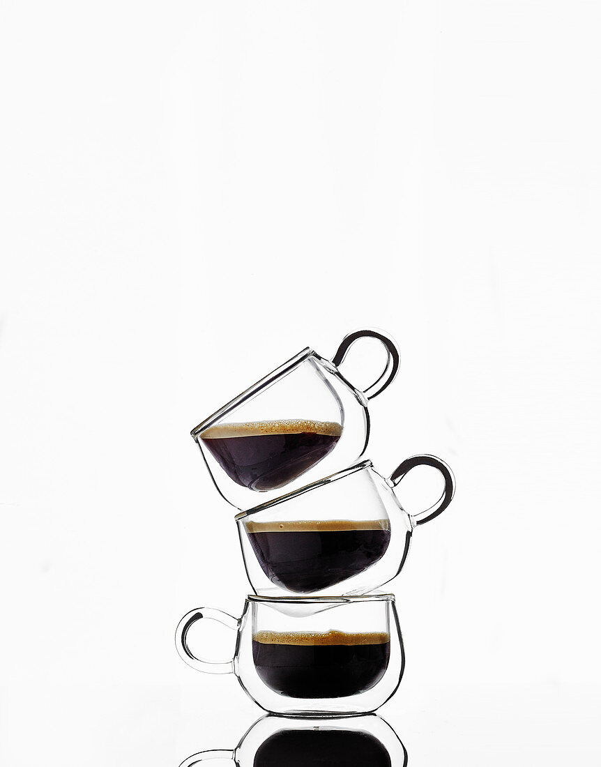 Drei Glastassen mit schwarzem Kaffee gestapelt vor weißem Hintergrund