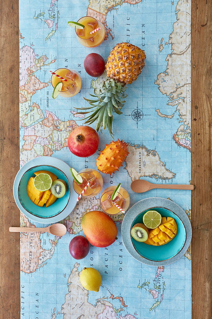 Fruity colored table with pineapple, kiwano, mango, passion fruit, lime, kiwi and pomegranate and world map