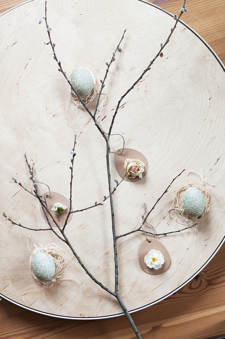 Liegende Osterdeko mit Zweig, Ostereiern, Rosenblüte, Narzissenblüte und Waxflower