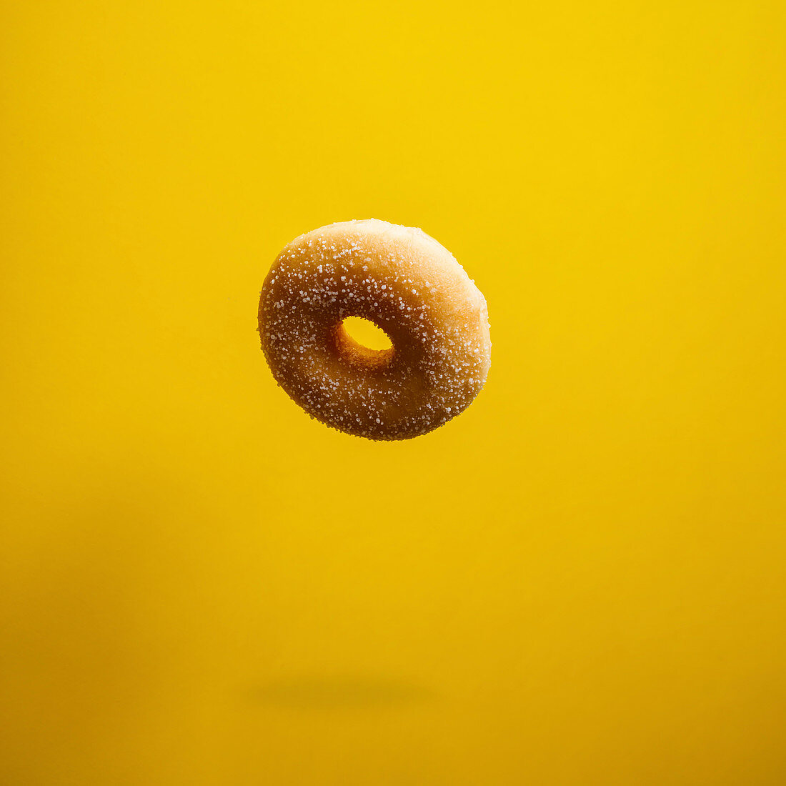 Sugar doughnut falling on yellow background