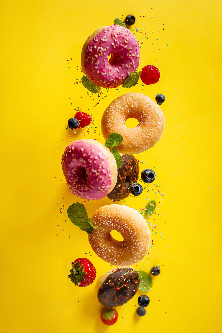 Various decorated doughnuts with sprinkles and berries falling on yellow background