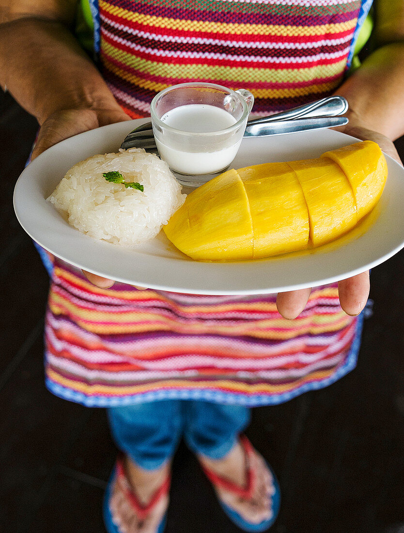 Frau serviert Thai-Mango mit Klebreis mit Kokosmilch
