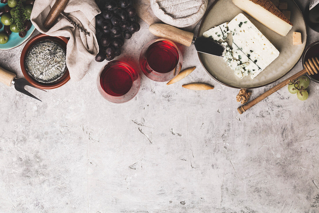 Zwei Gläser Rotwein, Käse, Trauben und Oliven auf Steinuntergrund