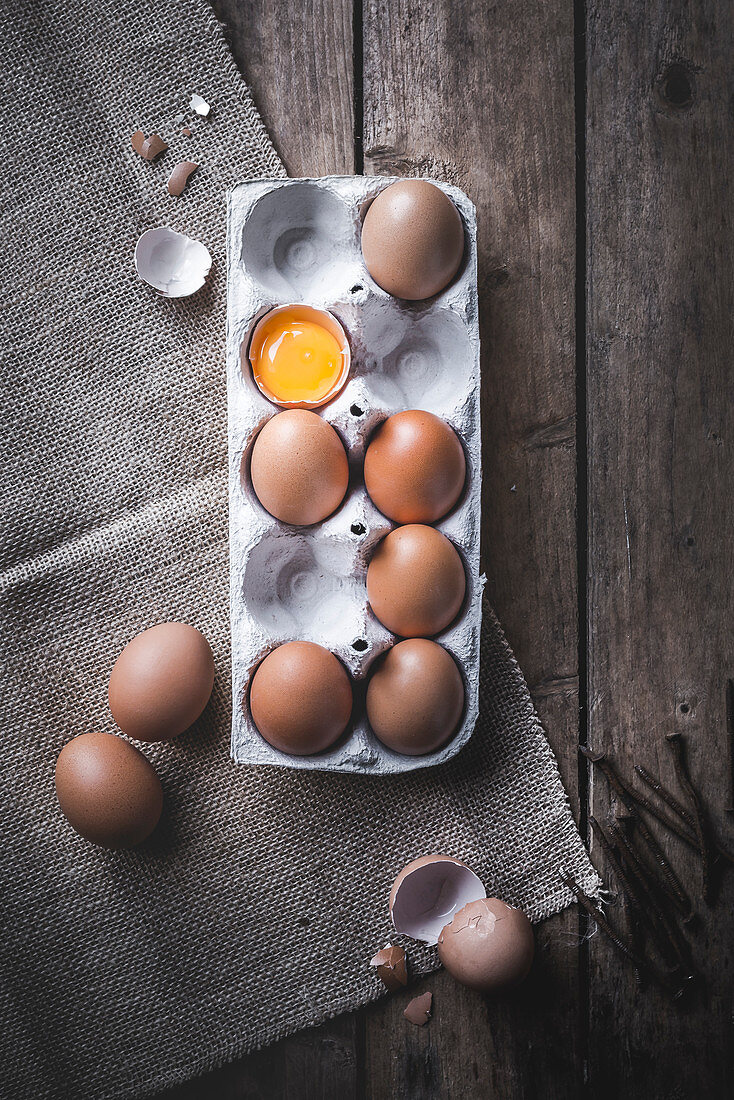 Fresh eggs in an egg carton, one cracked open