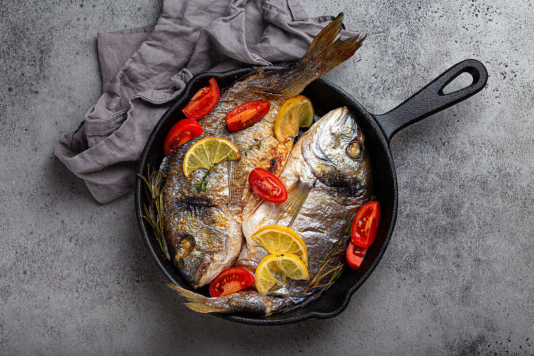 Gebratene Seebrassen mit Zitrone, Tomaten und Kräutern in der Pfanne