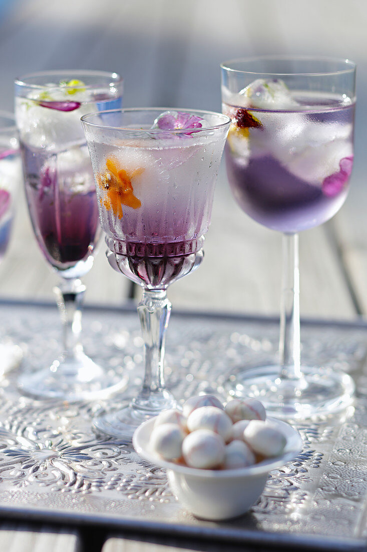 Three cocktail glasses with blueberry syrup and flowers ice cubes