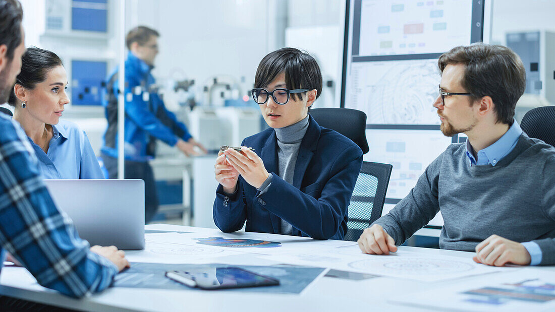 Engineer holding a circuit board in a team meeting