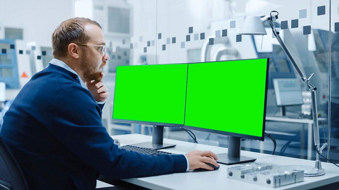 Industrial engineer using a computer with two green monitors