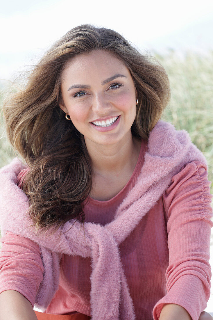 A young, long-haired woman wearing a pink blouse with a jumper over her shoulders