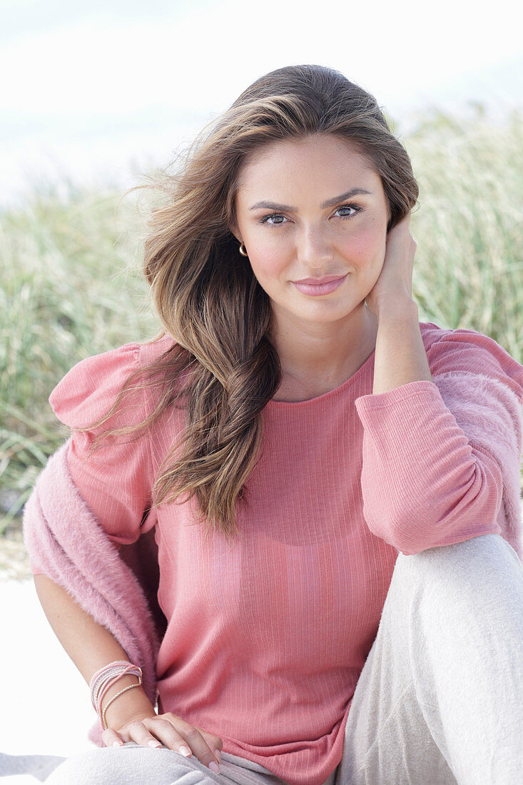 A young, long-haired woman wearing a pink blouse and light trousers