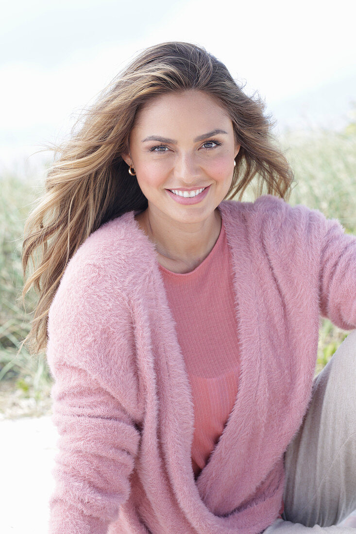 A young, long-haired woman wearing a pink blouse and a pink wrap-around jumper