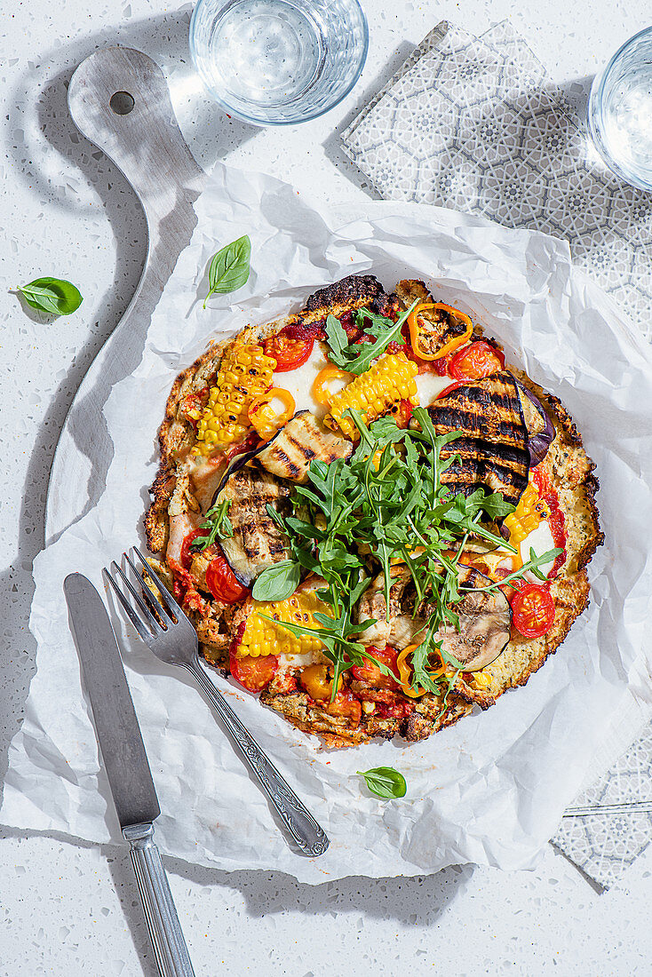 Low carb pizza made with cauliflower base, mozzarella cheese, tomatoes, aubergine, peppers, corn and rocket salad