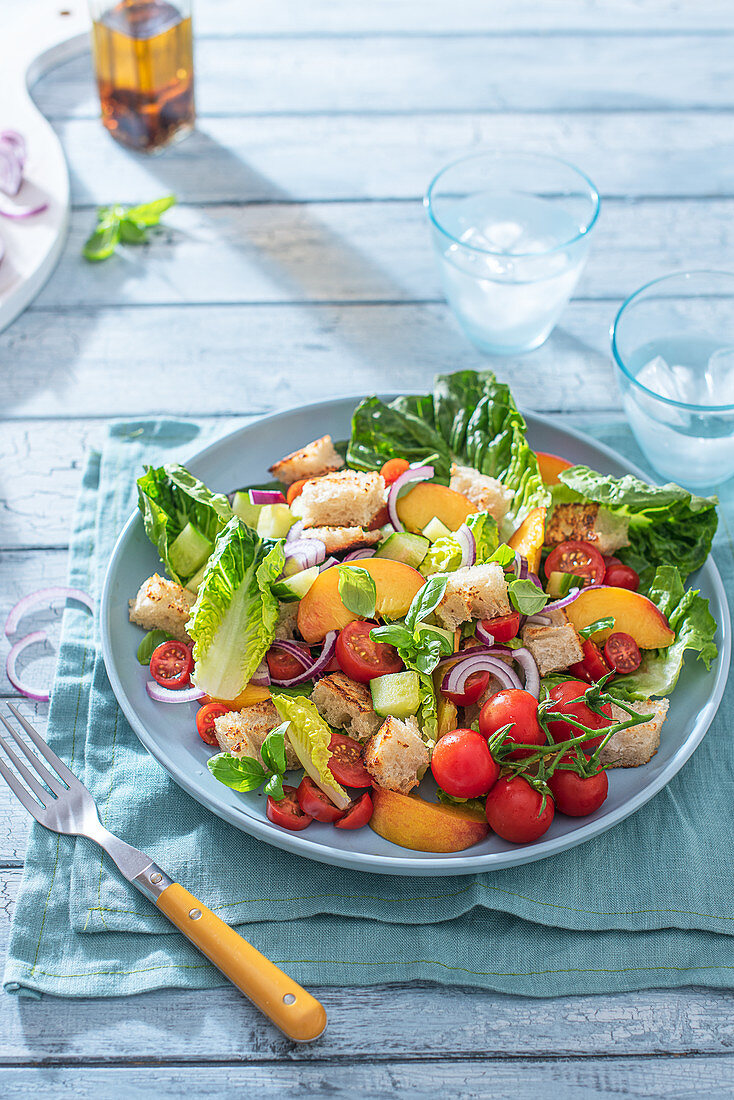 Panzanella salad with bread croutons, tomatoes, cucumber, red onions, peaches, lettuce, basil and oiive oil