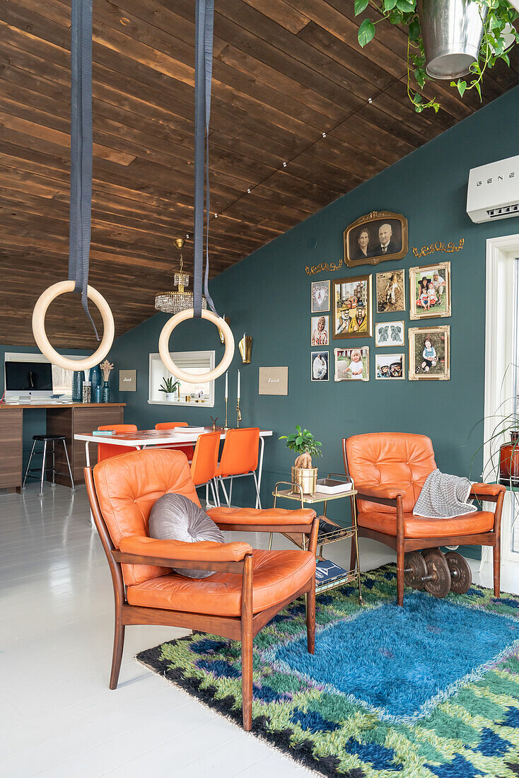 Armchairs with leather upholstery below gymnastic rings in living room with rustic wooden ceiling