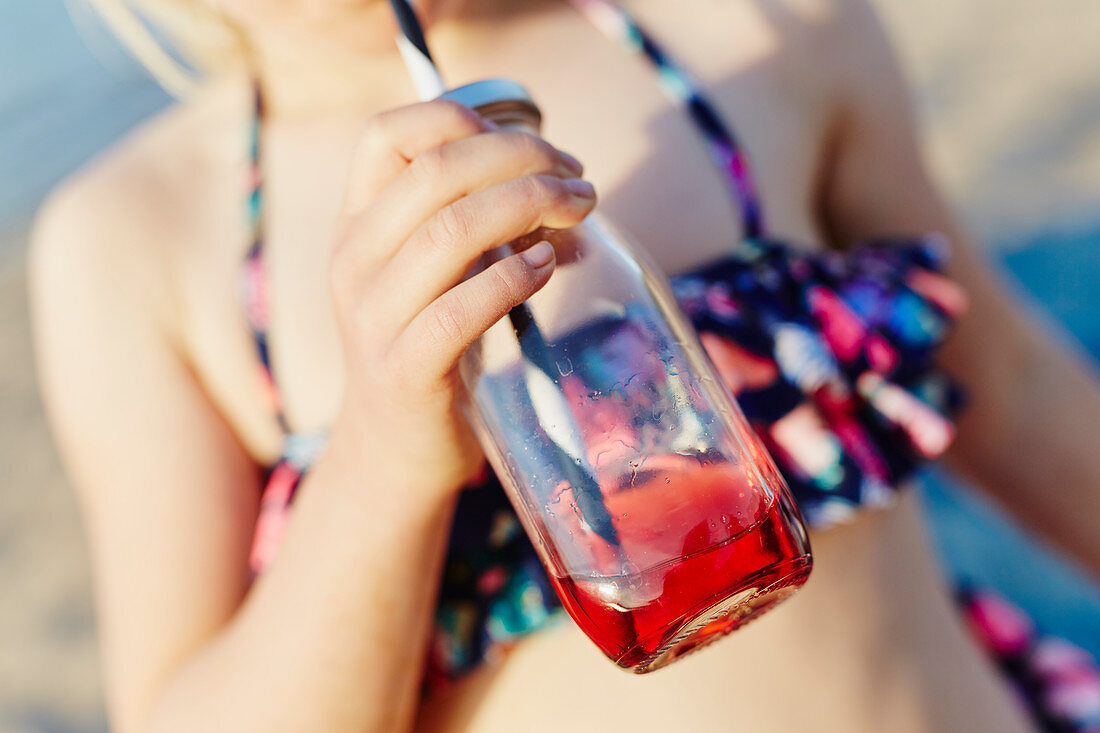 Mädchen trinkt am Strand aus Flasche