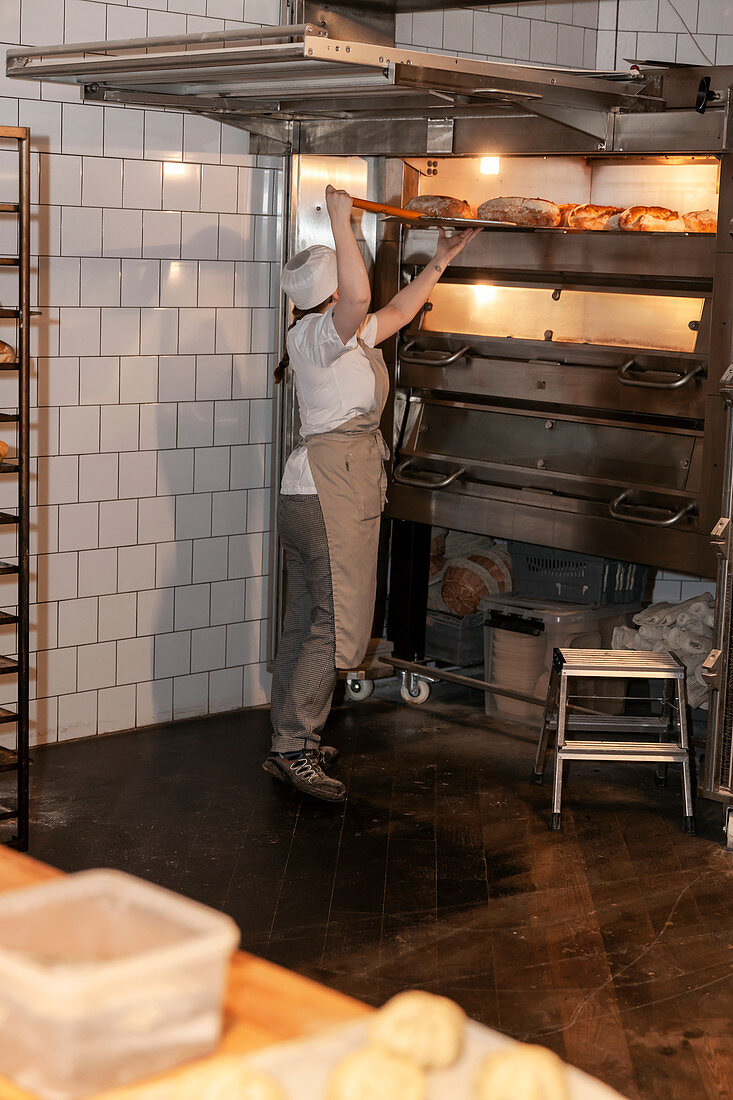 Bäckerin in Großbäckerei nimmt Brot aus dem Ofen