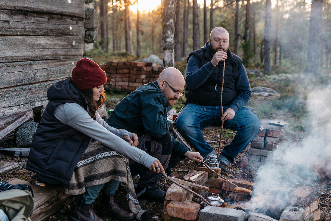 People preparing sausages over log fire