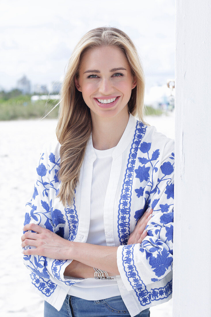 A long-haired blonde woman wearing a white t-shirt and a blue-and-white jacket