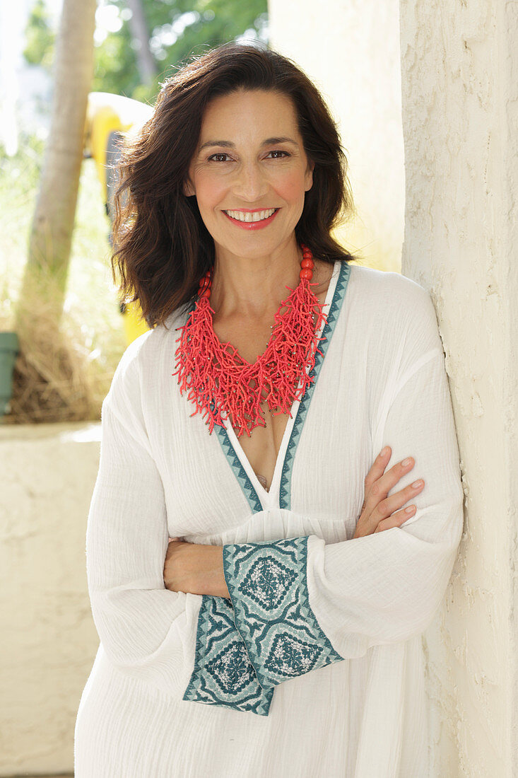 An older brunette woman wearing a statement necklace and a white dress with trim