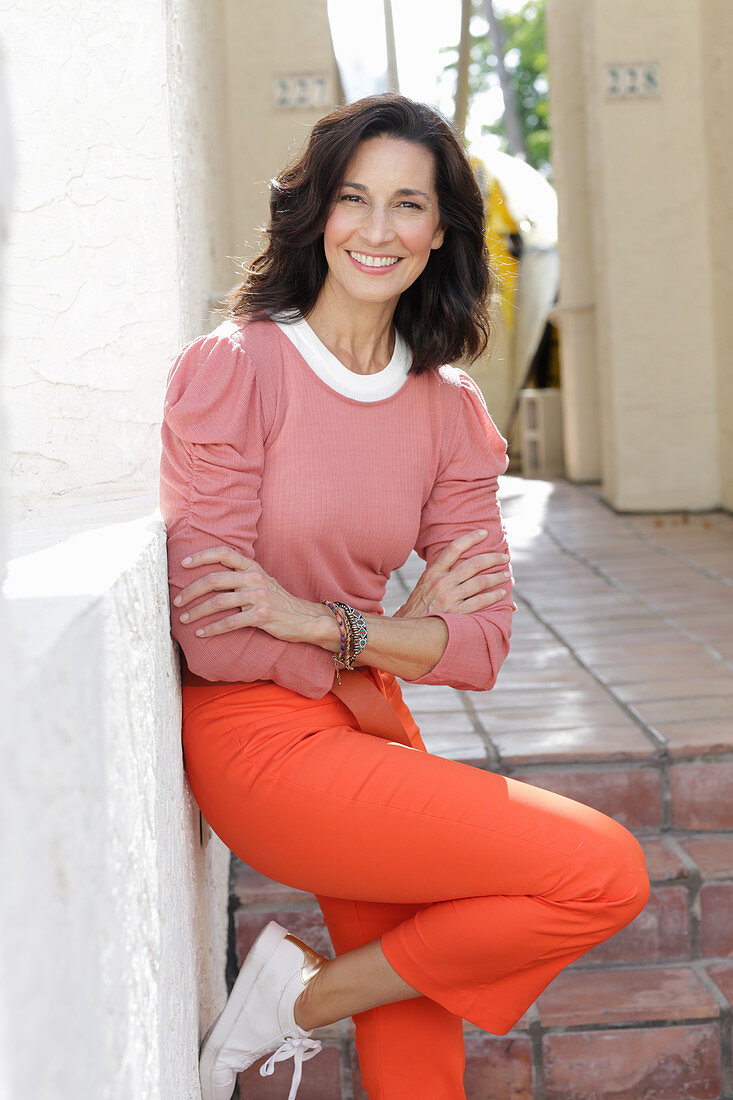 An older brunette woman wearing a pink top and orange trousers