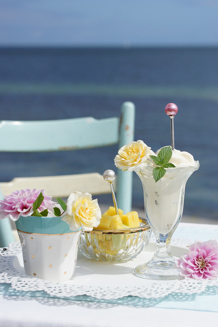 Vanilleeis in Becher mit Rosenblüte dekoriert, im Hintergrund Ananasstücke im Schälchen