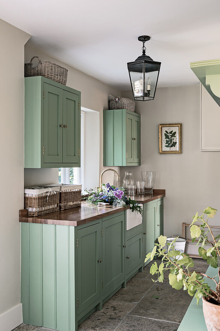 Cut flowers in Belfast sink with green painted fitted units in Georgian family home.